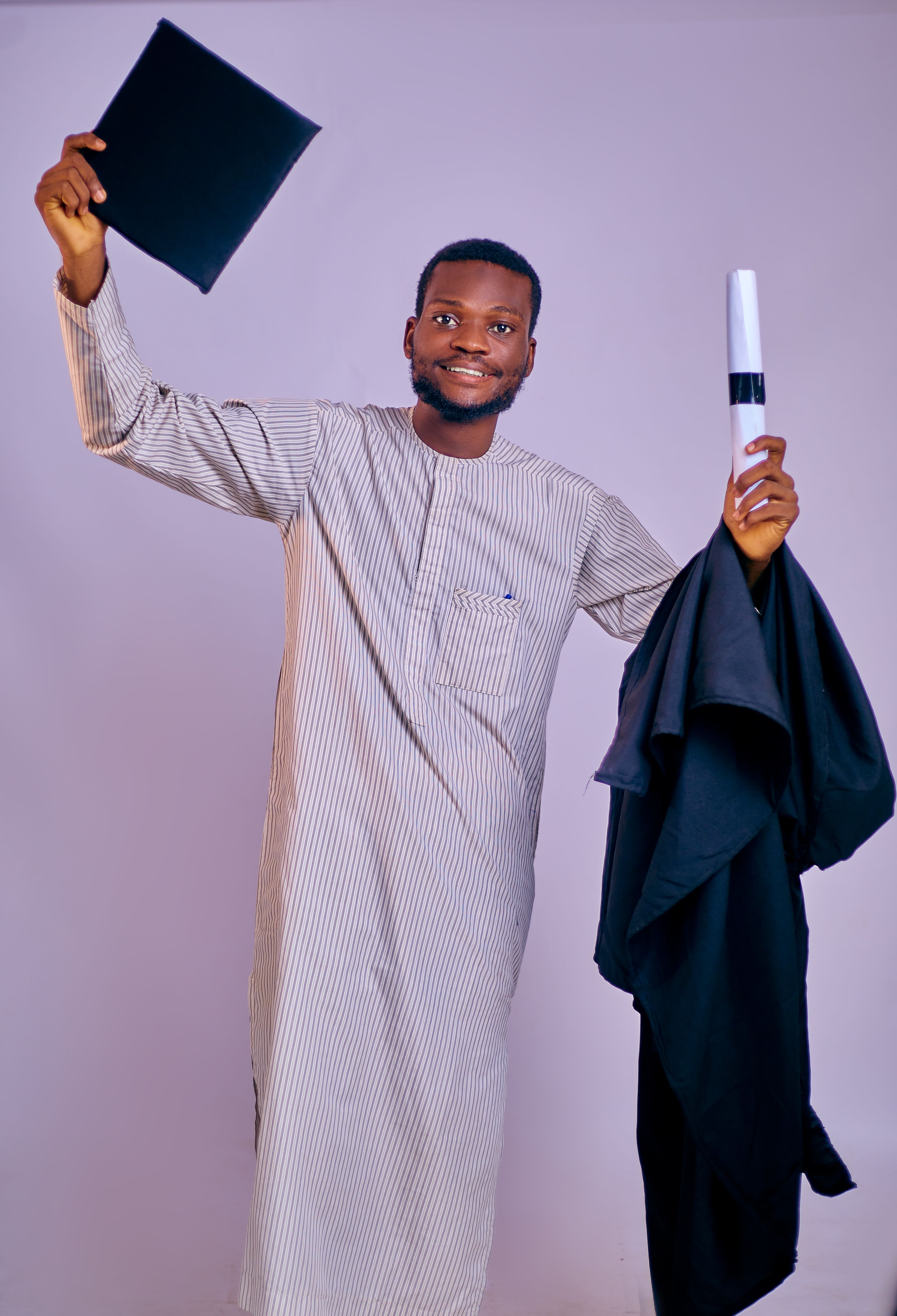 Smiling young man in traditional attire celebrating graduation holding a diploma and cap.