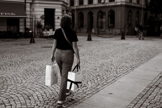 Woman walking on cobblestone street with shopping bags in Stockholm.