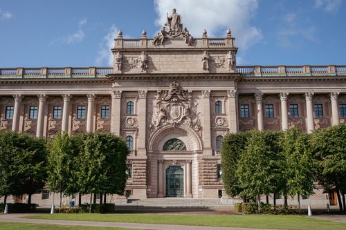 Free Elegant facade of Stockholm's Parliament House with clear blue skies and lush greenery. Stock Photo