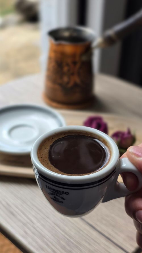 Free Hand holding Turkish coffee cup with traditional pot on a wooden table, creating a cozy atmosphere. Stock Photo