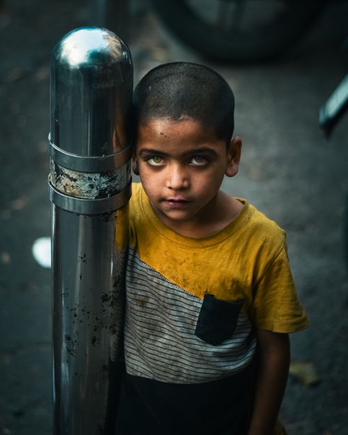 Free A young boy in a yellow shirt leans against a metal post on a street in Pune, India, showcasing vivid eyes. Stock Photo
