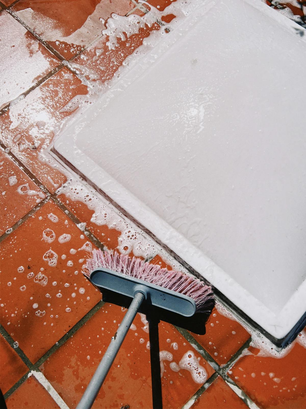 Persona che strofina piastrelle esterne con spazzola e schiuma di sapone