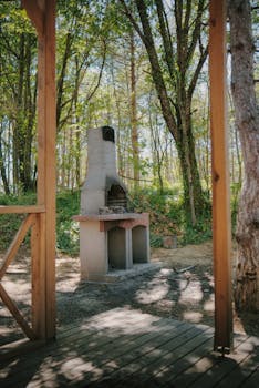 A rustic barbecue stands amidst a tranquil forest setting during a sunny summer day.