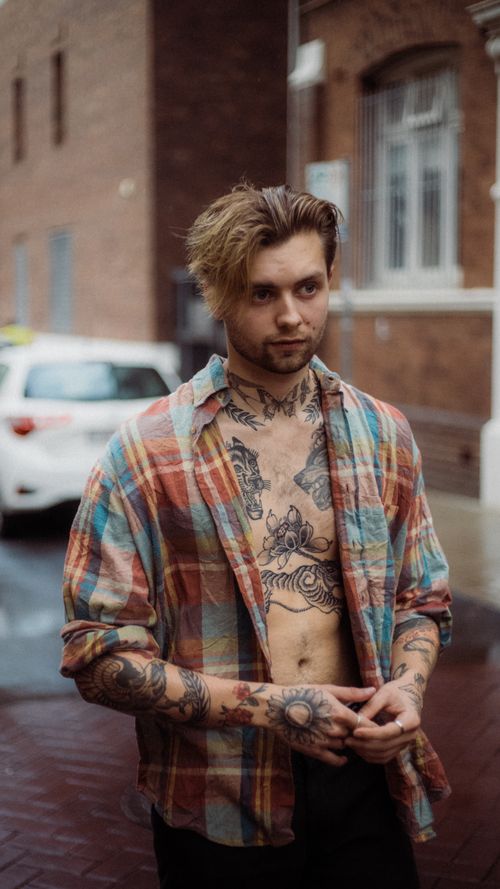 Free Portrait of a young man with tattoos and casual attire posing in an urban setting. Stock Photo