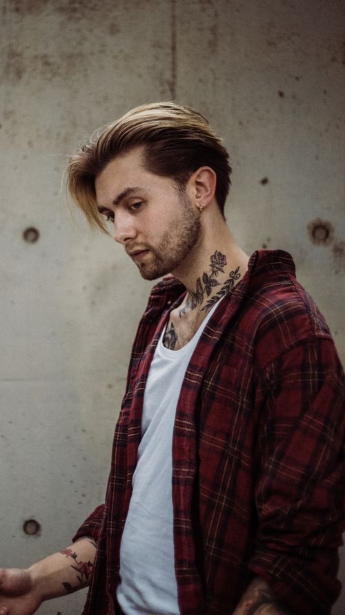 Free Stylish young man with tattoos wearing a plaid shirt, looking pensive. Stock Photo