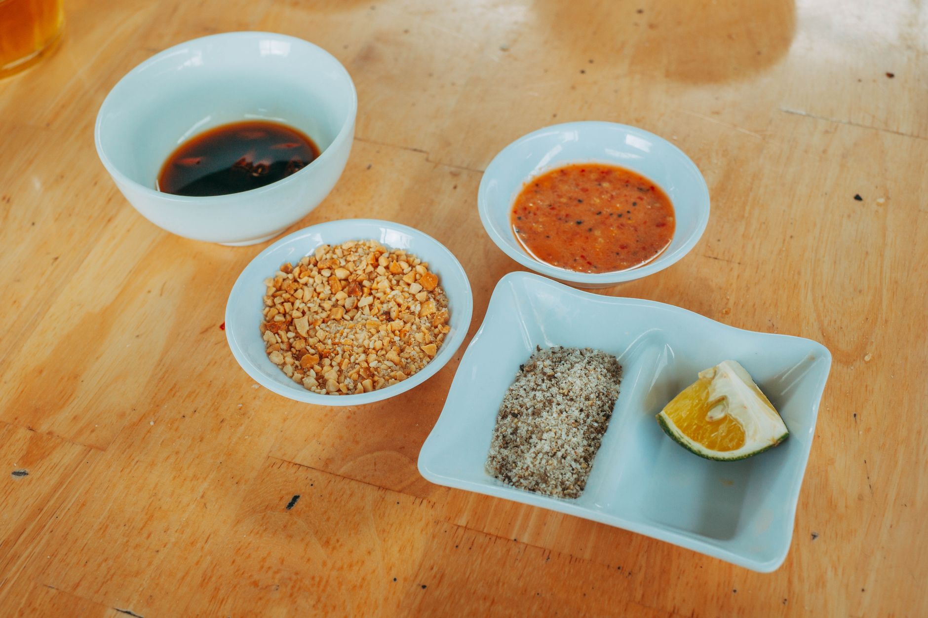 Variety of condiments including lime, peanuts, and sauces on a wooden table.