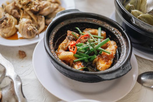Appetizing Asian chicken dish in clay pot garnished with chilies and vegetables, perfect for culinary presentations.