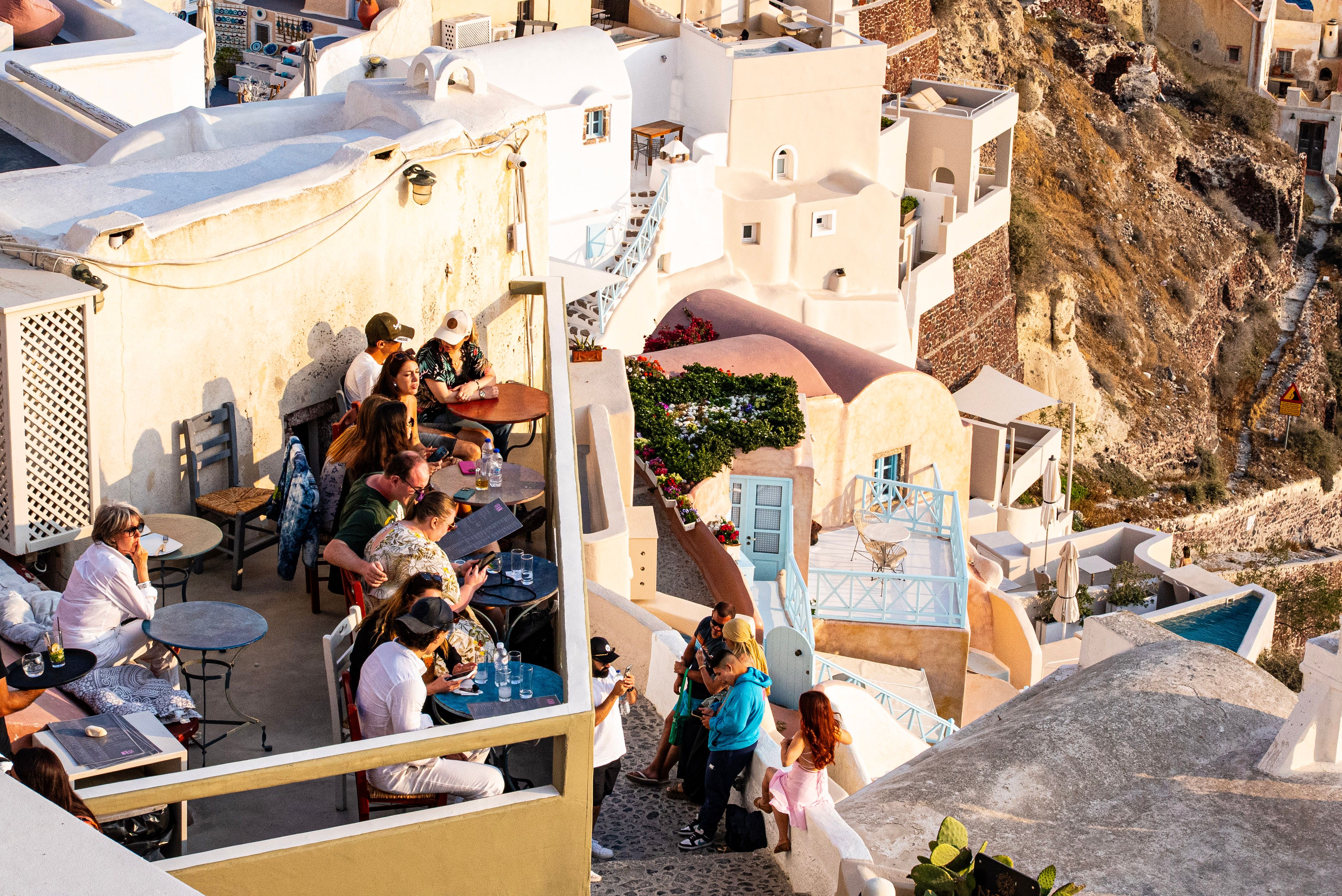 Vibrant terrace scene overlooking Santorini's iconic architecture during a warm summer sunset in Fira, Greece.