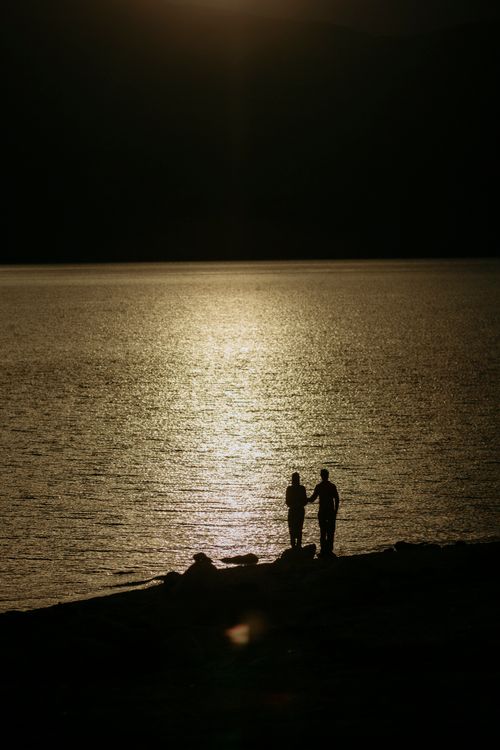 Free Silhouettes of two people walking by a tranquil lake at sunset. Stock Photo