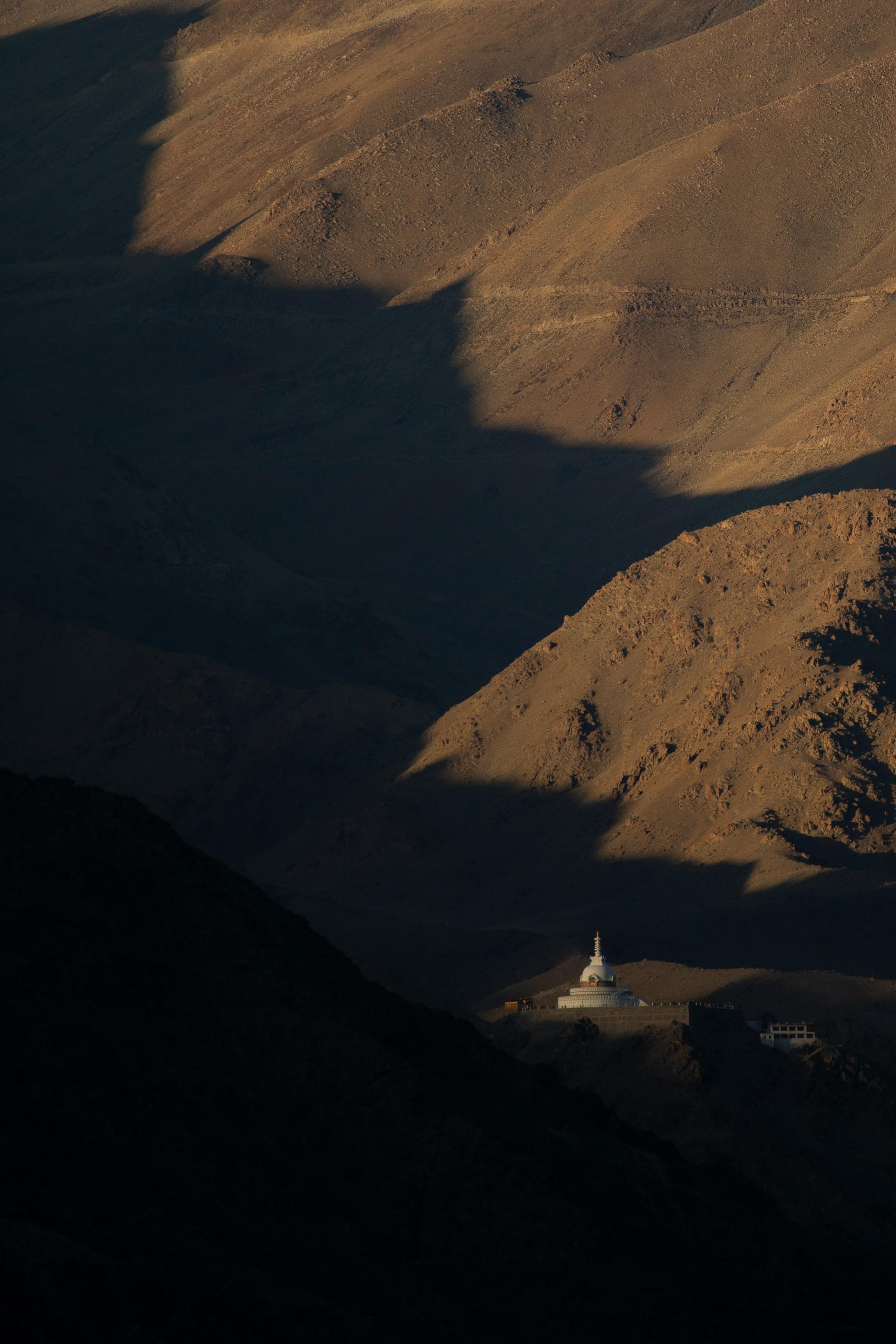 Dramatic shadows cast over Leh's mountainous terrain with a visible stupa.