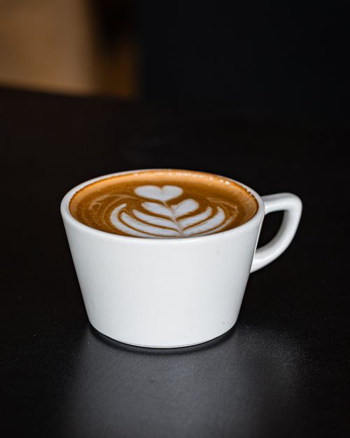 Free Close-up of an artistic latte with intricate foam design in a white cup on a dark table, perfect for coffee lovers. Stock Photo