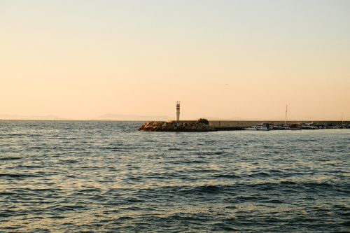 Free Serene sunset lighthouse scene on a rocky breakwater with calm ocean waves. Stock Photo