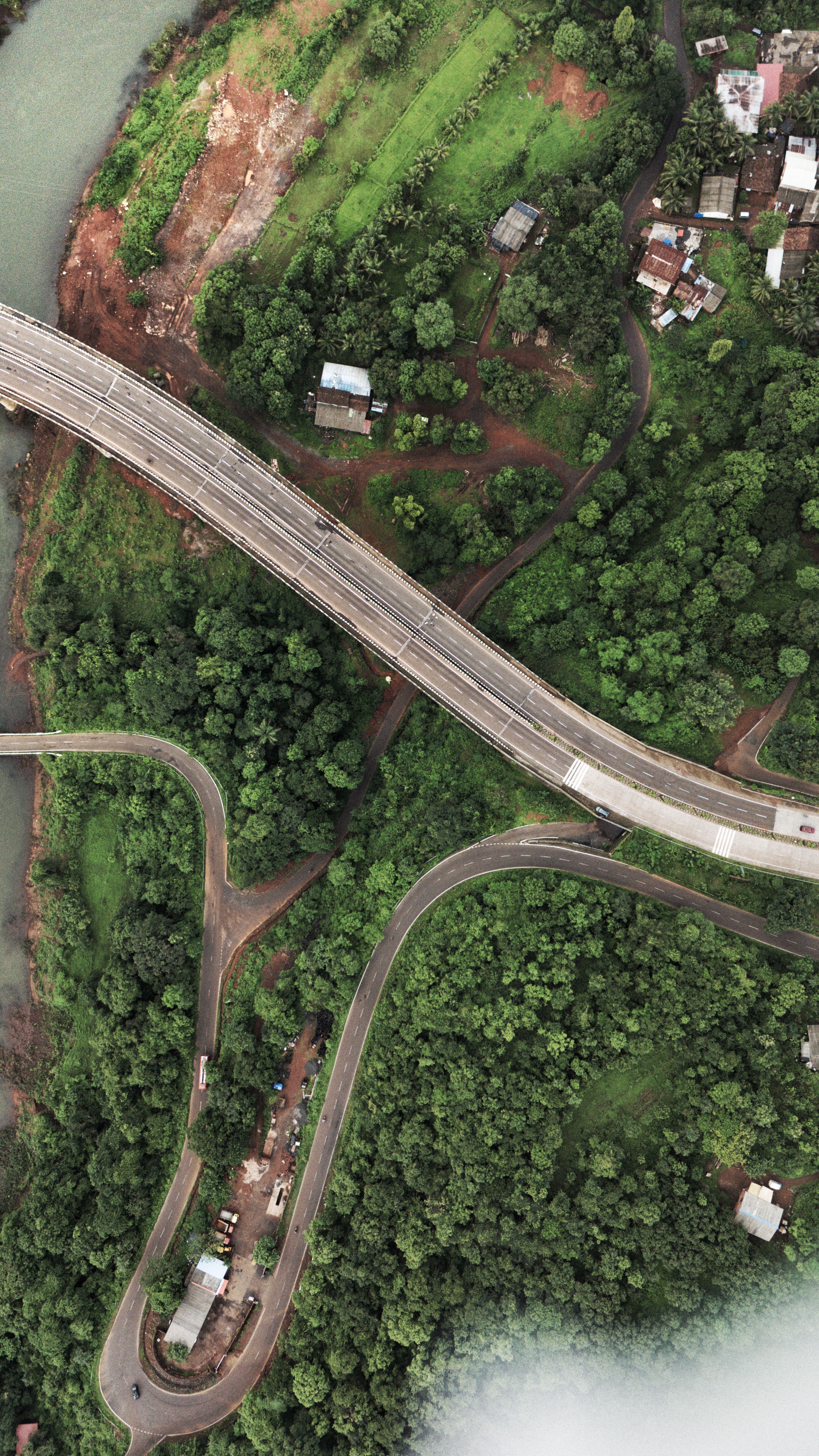 Aerial shot of a winding road and bridge through a lush green forest landscape.