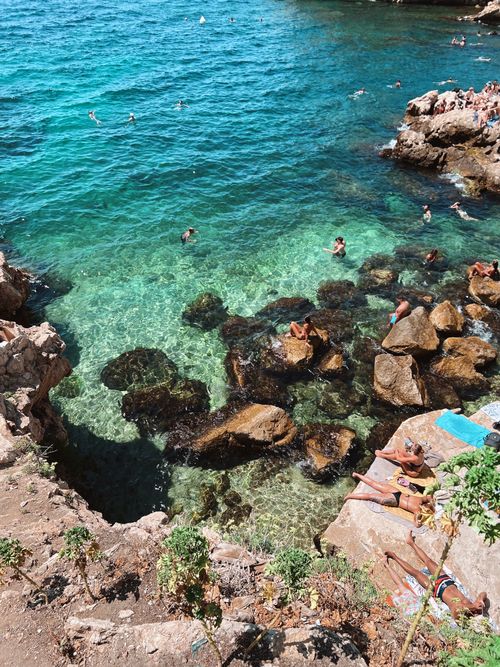 Free People enjoying a rocky seaside with clear blue water and sunbathers on rocks. Stock Photo