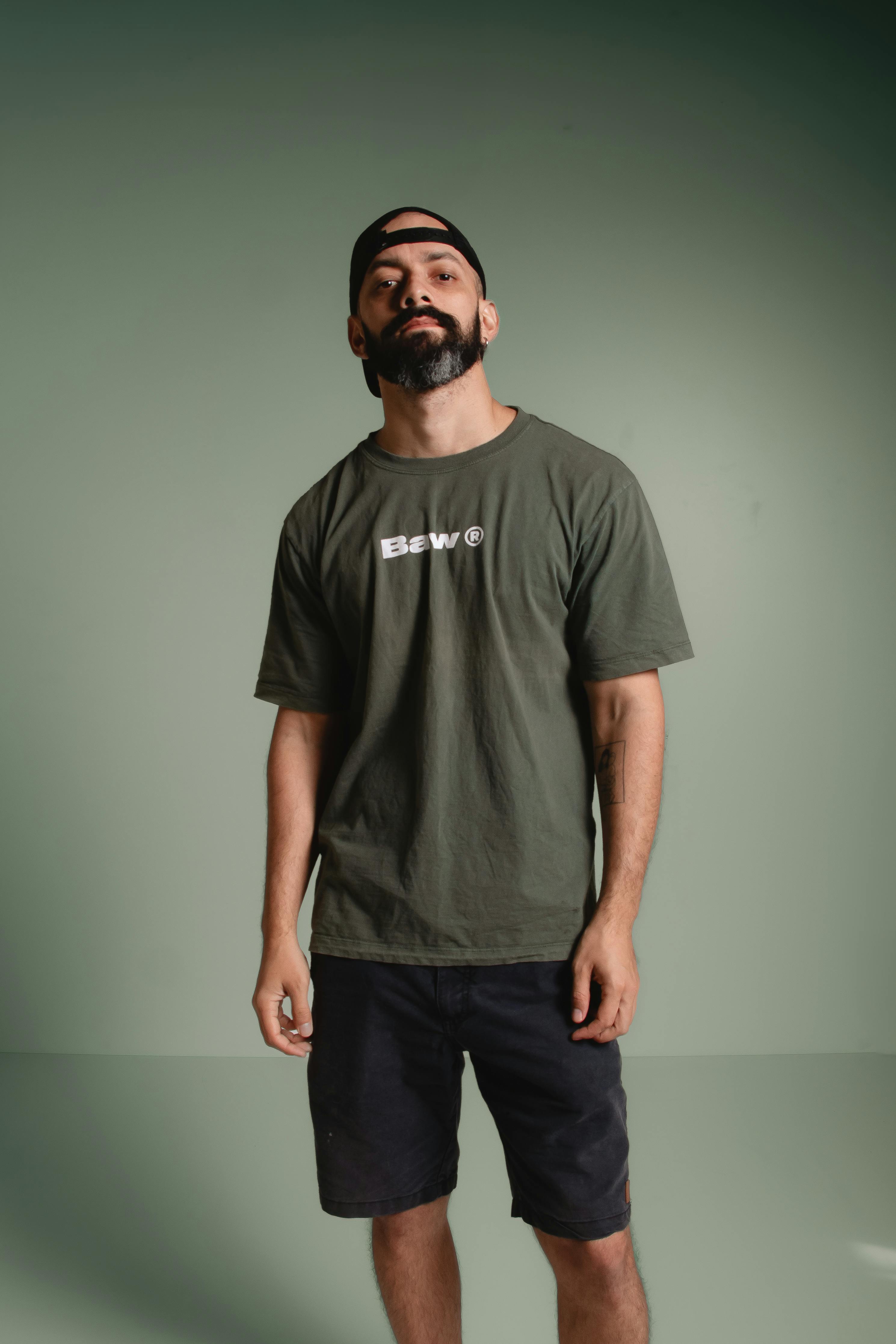 grátis Retrato casual de um homem em pé, confiante, contra um fundo verde, usando um boné e uma camiseta verde. Foto profissional