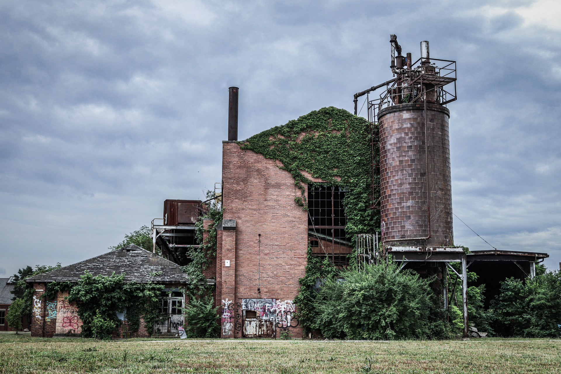 Rustic abandoned factory covered in ivy with storm clouds above, offering a moody industrial scene.