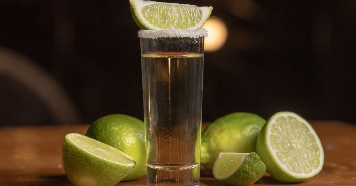 A classic tequila shot with a lime wedge and salt rim on a wooden table.