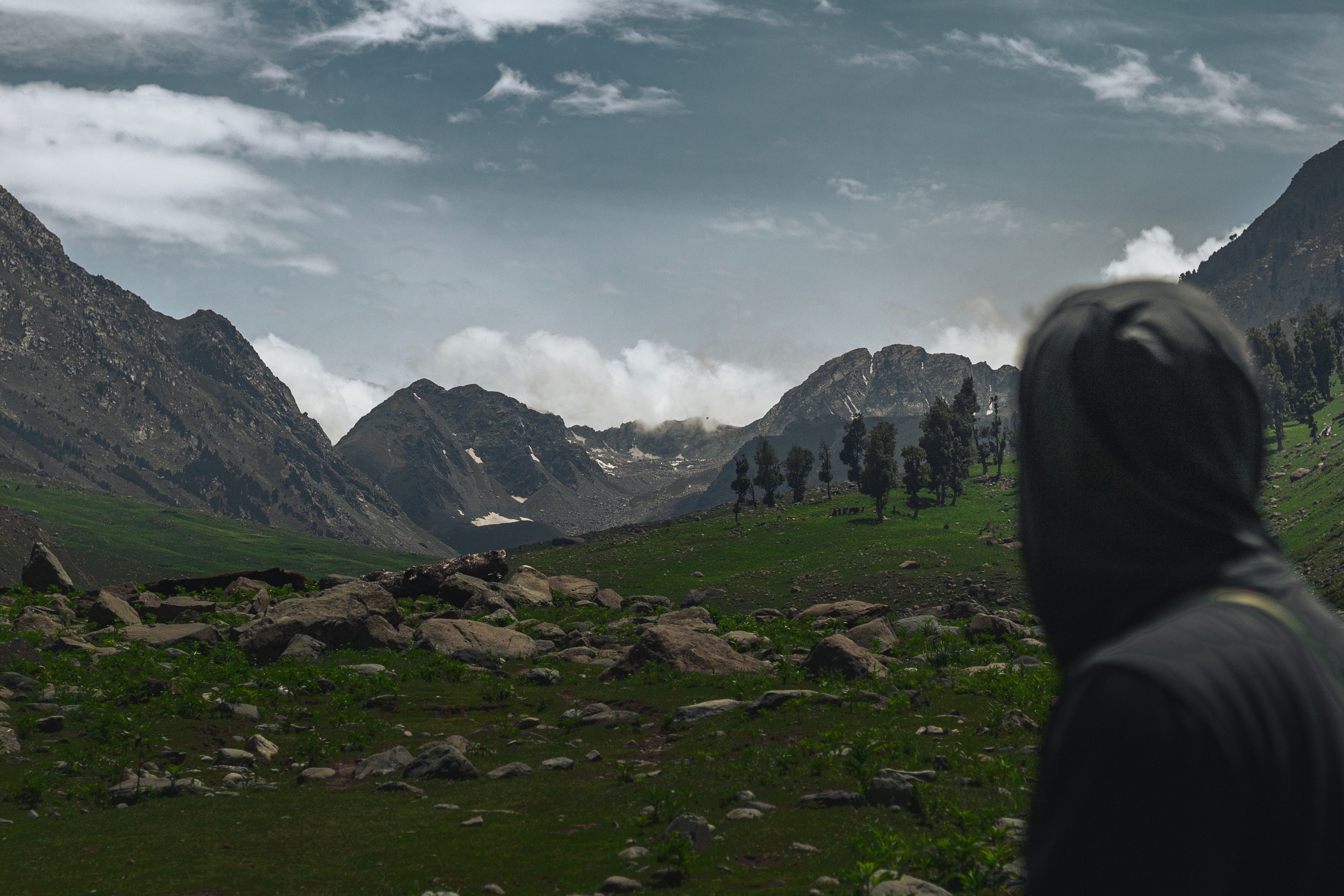 A lone hiker in a hoodie gazes at a scenic mountain valley on an overcast day.