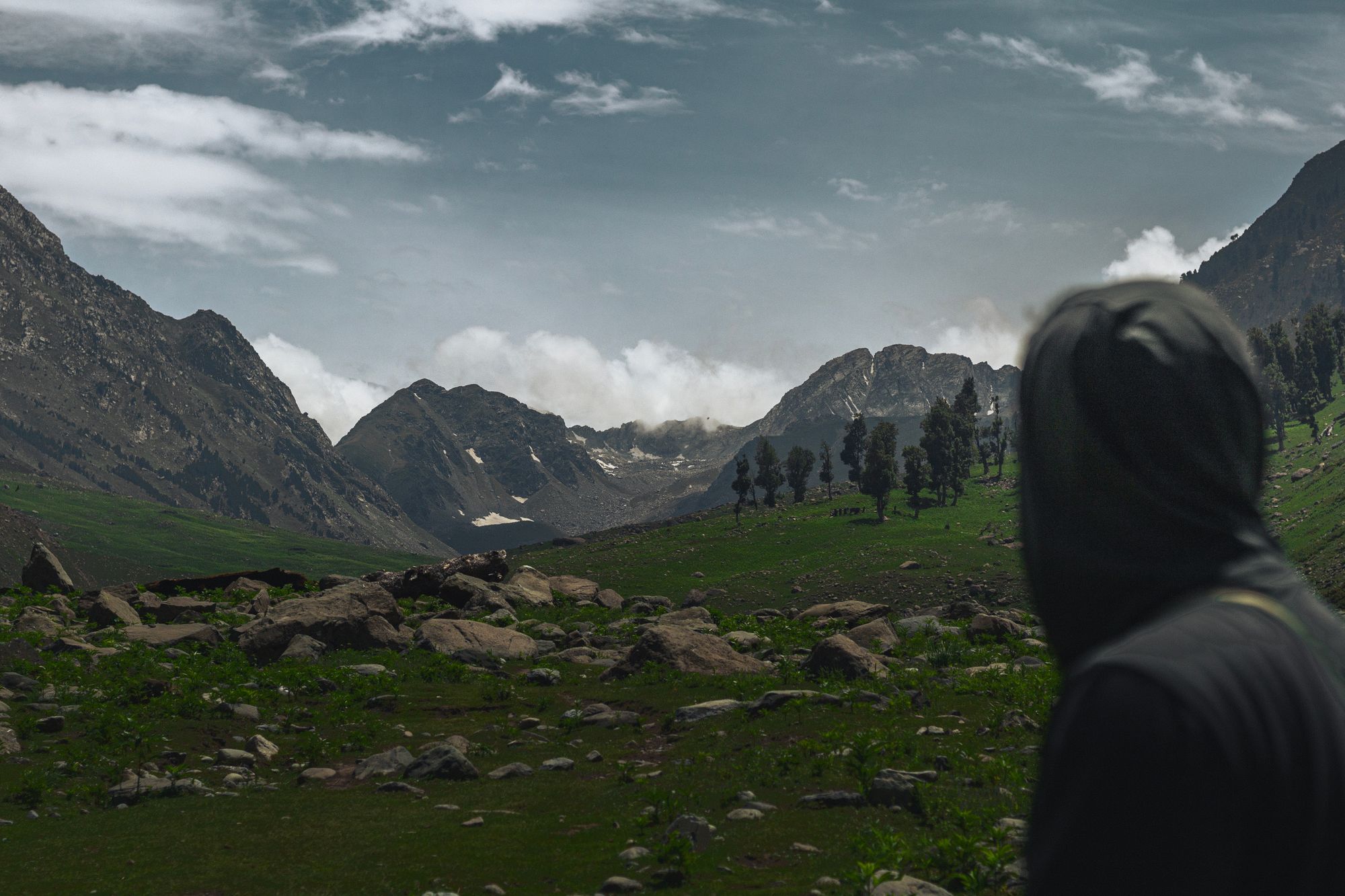 A lone hiker in a hoodie gazes at a scenic mountain valley on an overcast day.