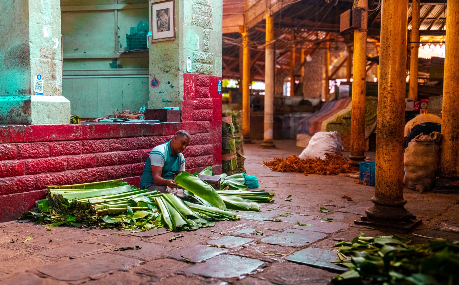 A vendor prepares banana leaves for sale in an Indian market, showcasing vibrant colors and textures.