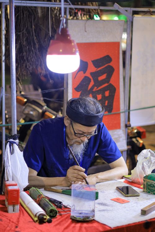 Free Elderly Vietnamese calligrapher creating art in a vibrant night market setting. Stock Photo