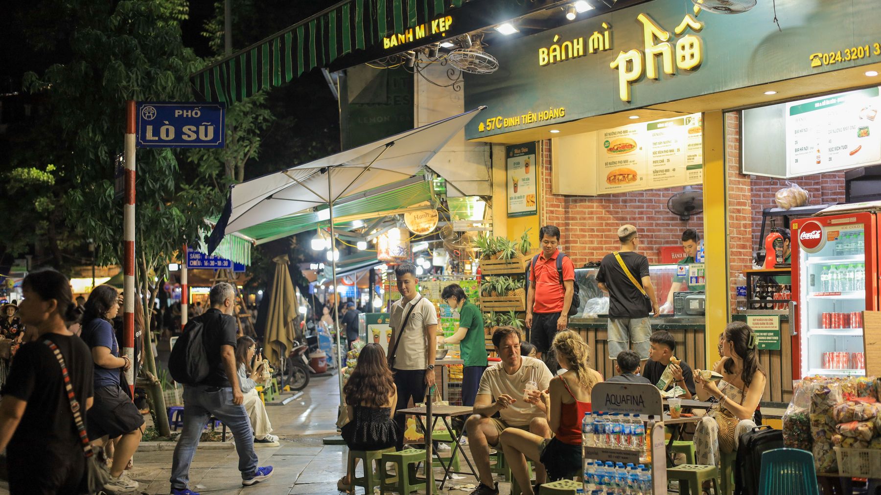 Vibrant night scene of people enjoying street food outside a Vietnamese sandwich shop in Hanoi.