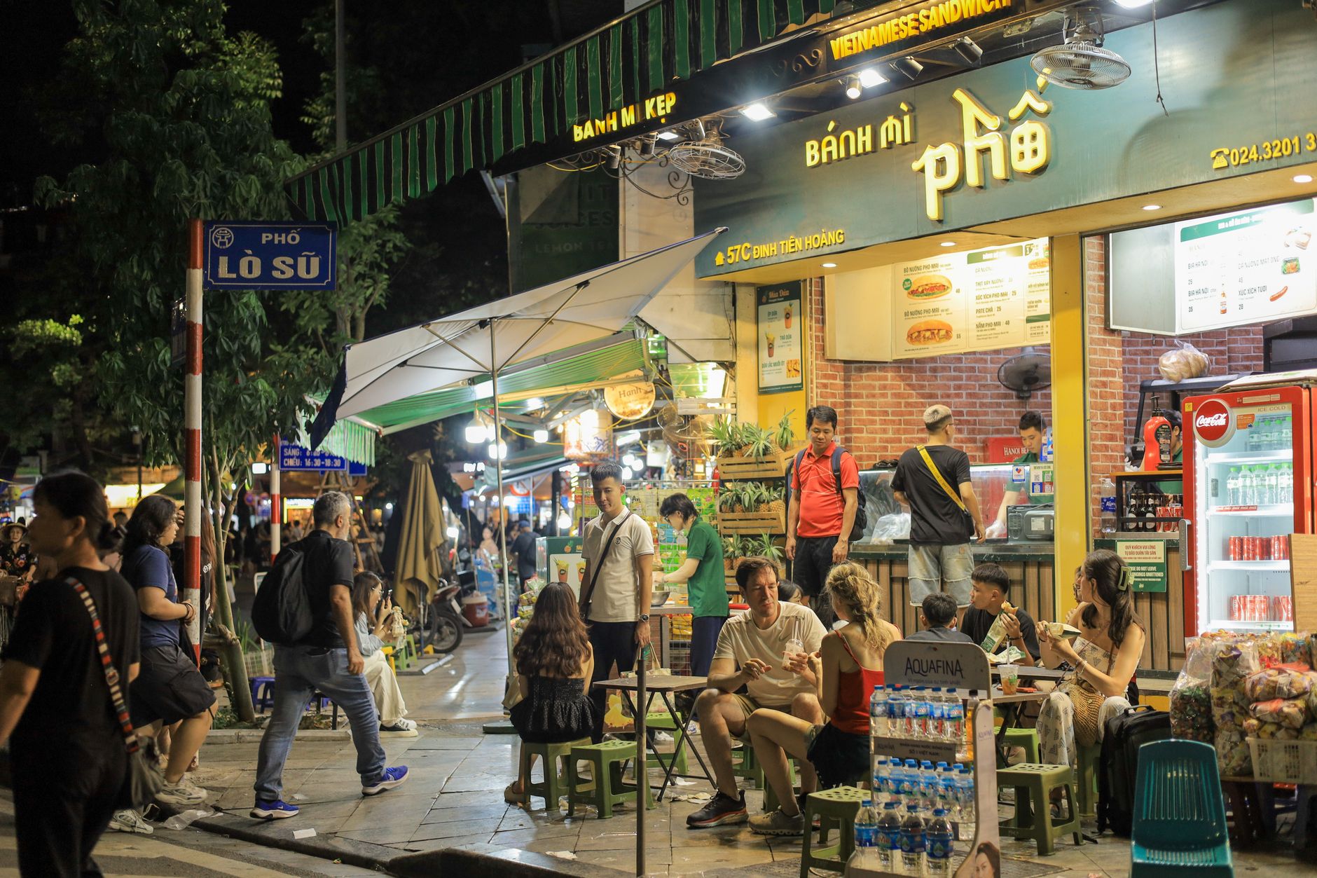 Vibrant night scene of people enjoying street food outside a Vietnamese sandwich shop in Hanoi.