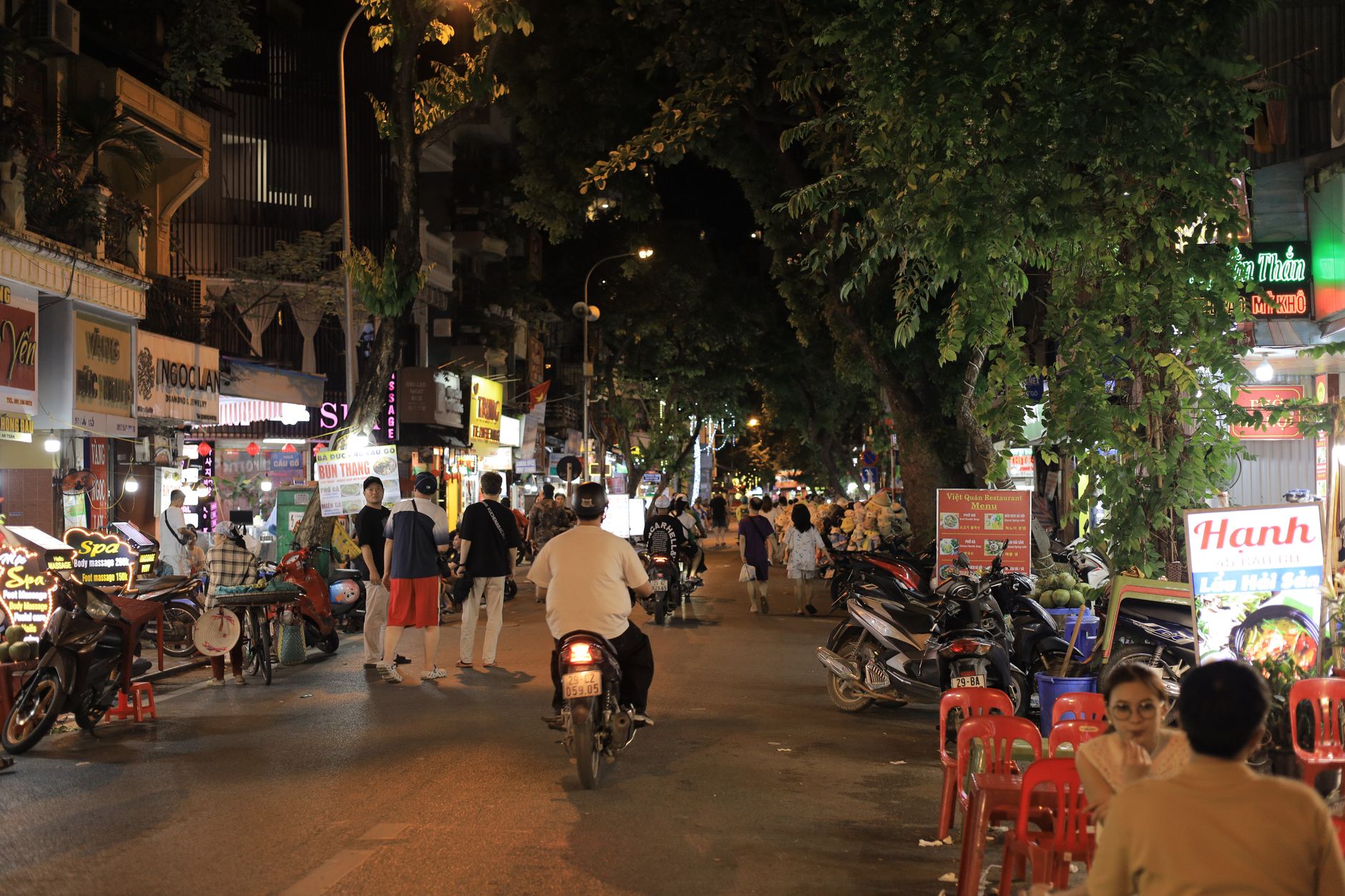 Vibrant street scene in Vietnam's nightlife with people, scooters, and illuminated signs.