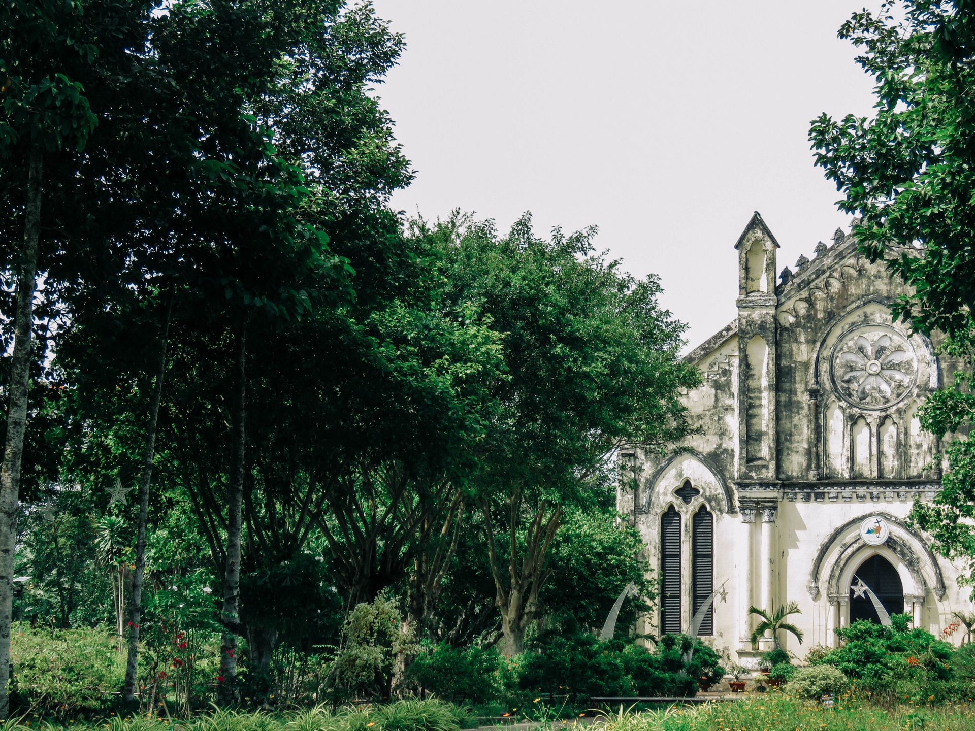 Gothic church facade surrounded by lush trees and shrubs in a serene outdoor setting.