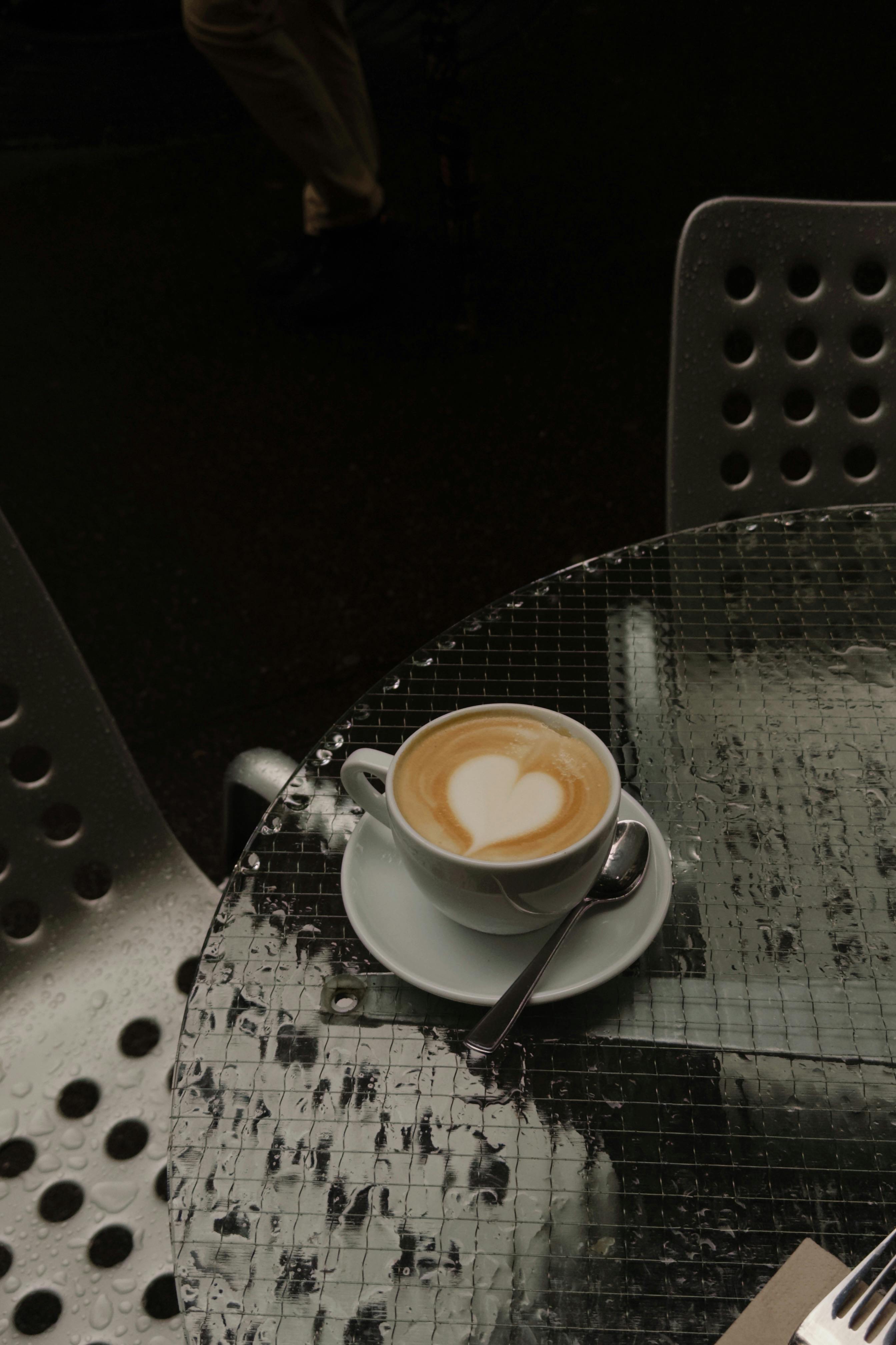 Warm latte with heart art on a rainy outdoor cafe table.