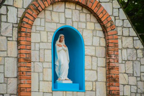 Free Statue of Virgin Mary in a stone niche with blue background and brick arch. Stock Photo