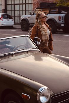 Stylish woman with dreadlocks by vintage convertible in Los Angeles.