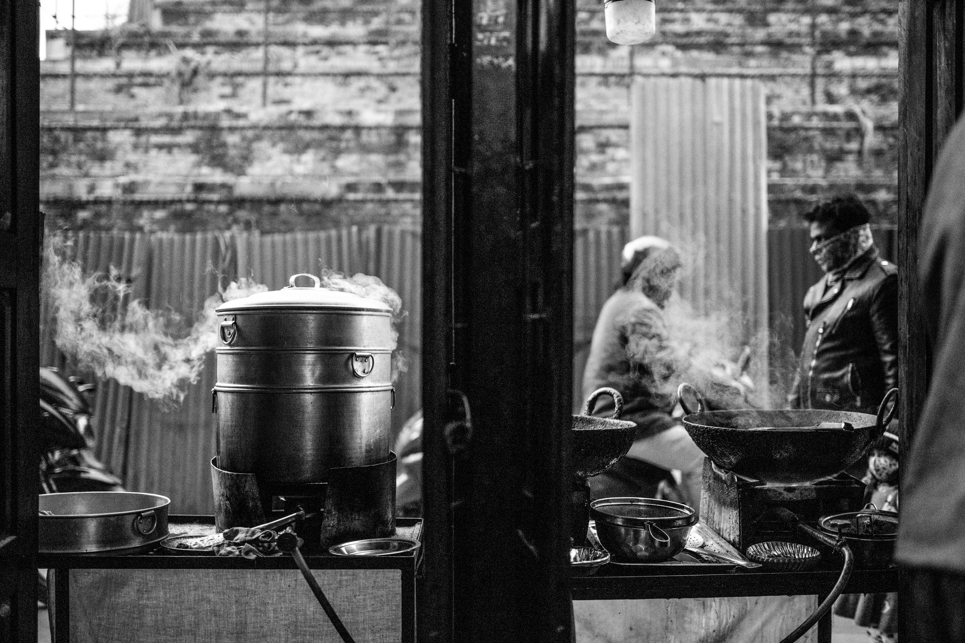 Black and white image of street food preparation in Kathmandu, Nepal, showcasing cooking pots and local life.