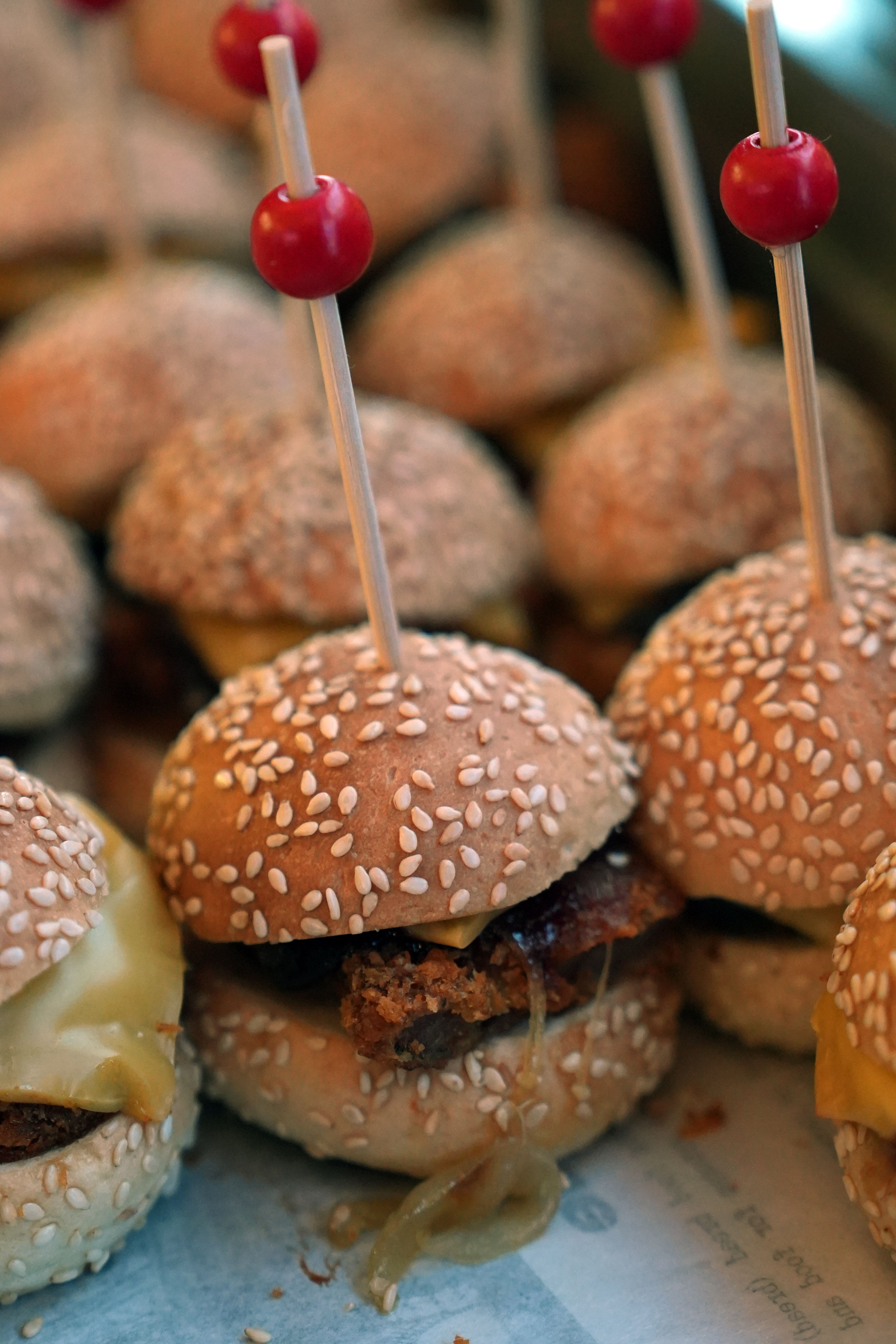 A mouthwatering close-up of mini cheeseburgers topped with sesame seeds and red skewers.