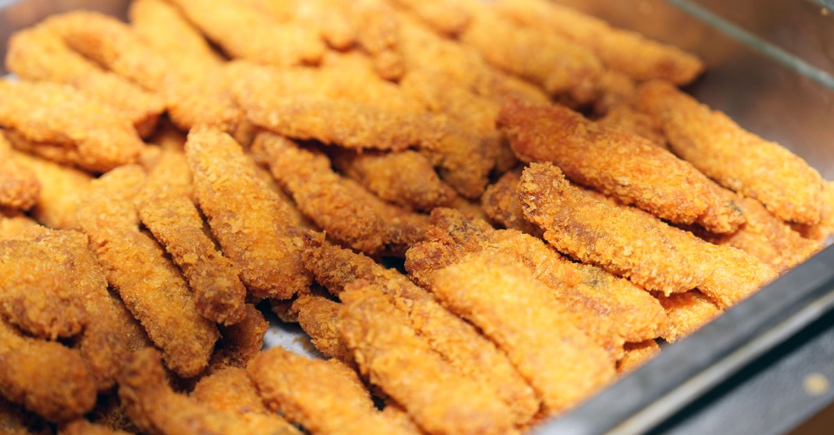 Palitos de peixe empanados e dourados, dispostos ordenadamente em uma bandeja de metal, perfeitos para bufês ou reuniões.