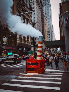 Street scene in New York City with steam rising from a vent amidst bustling pedestrians.