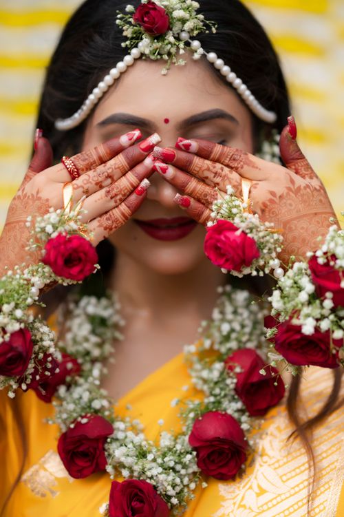 Free Beautiful Indian bride with floral jewelry and henna-covered hands covering her face in a traditional setting. Stock Photo