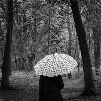 A woman with an umbrella walks through a rainy forest, capturing a serene moment in nature.