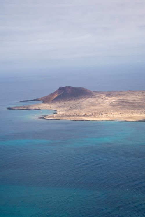 Free A stunning aerial shot of a volcanic island surrounded by the serene blue ocean. Stock Photo