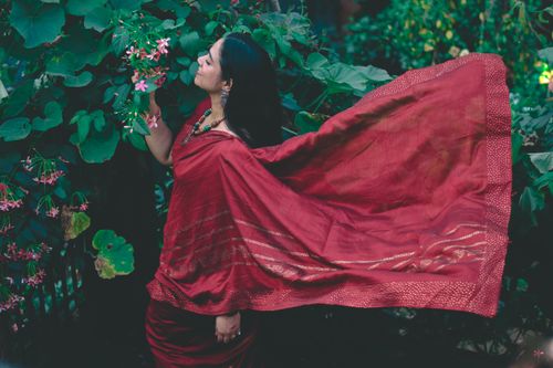 Free Woman in a flowing red saree stands among lush green foliage, embracing traditional Indian beauty. Stock Photo