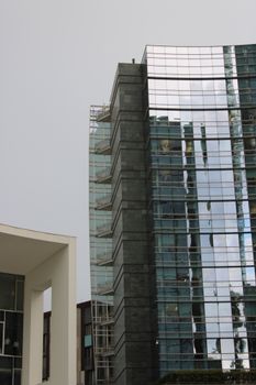 Contemporary glass skyscraper with reflections in Milan's vibrant urban landscape.