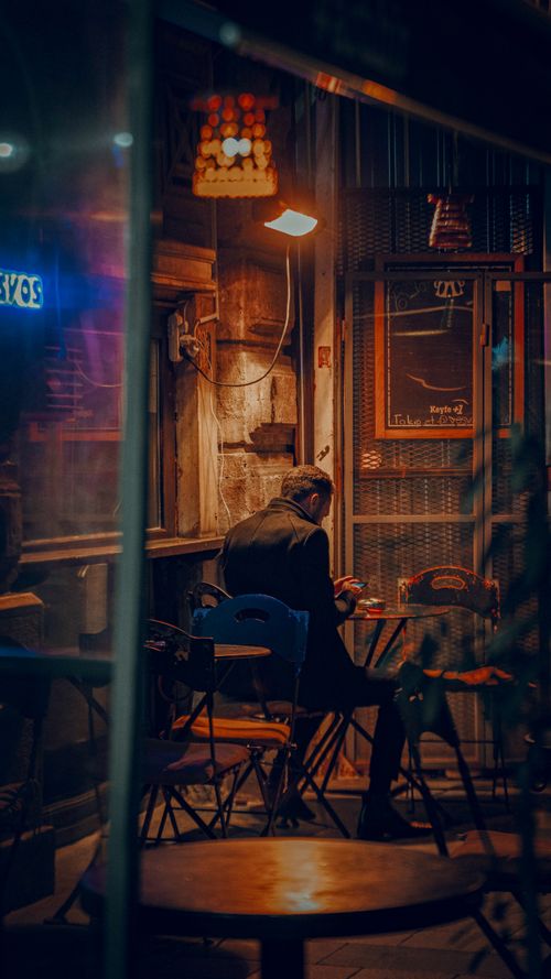 Free A solitary person enjoys a quiet evening at an Istanbul cafe, bathed in warm light. Stock Photo