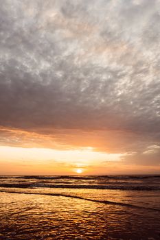 Golden sunset casting a warm glow over Middelkerke beach, Belgium, under dramatic clouds.