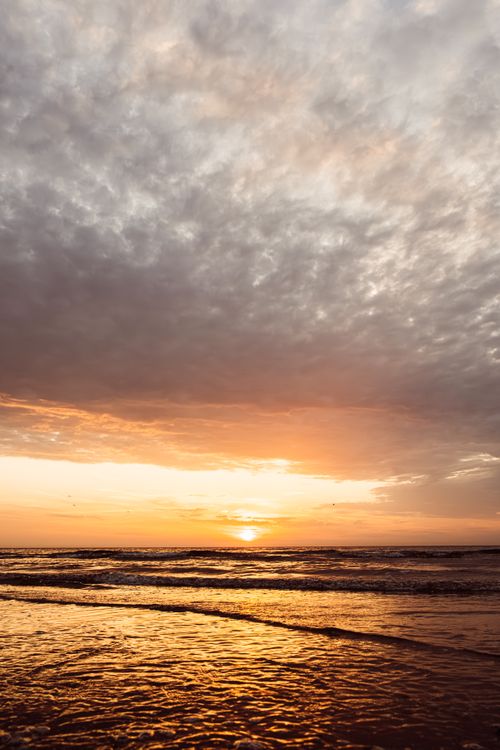 Free Golden sunset casting a warm glow over Middelkerke beach, Belgium, under dramatic clouds. Stock Photo