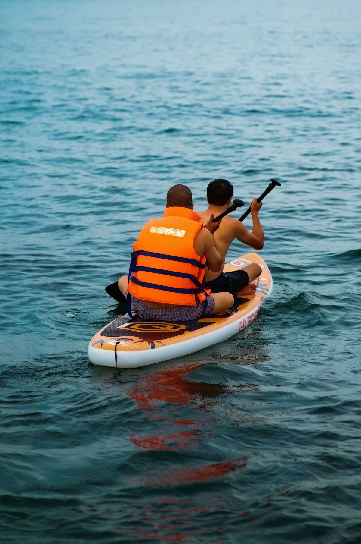Two people wearing flotation gear while paddleboarding on open water