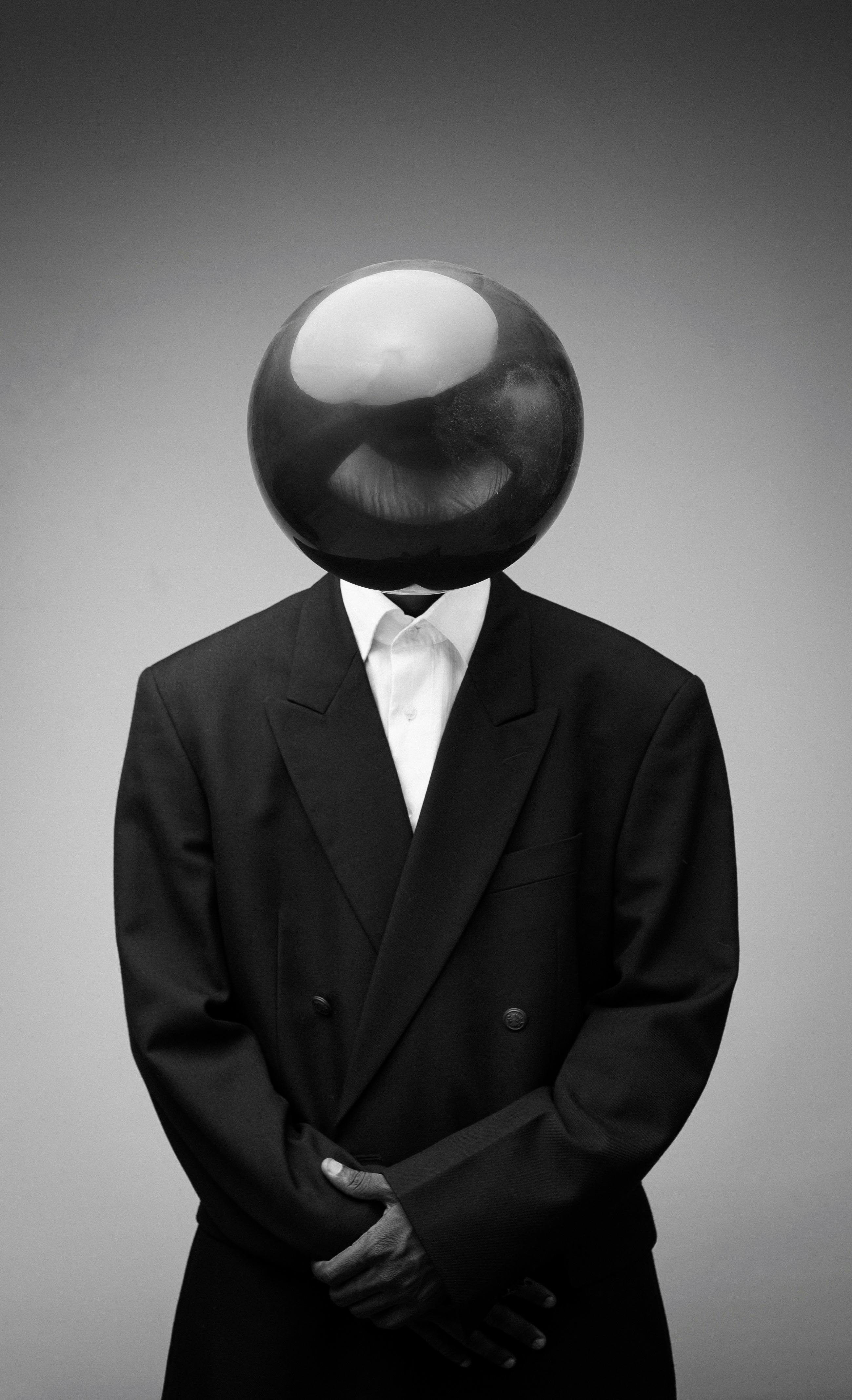 Black and white image of a surreal headless figure in a suit with a reflective sphere as a head.