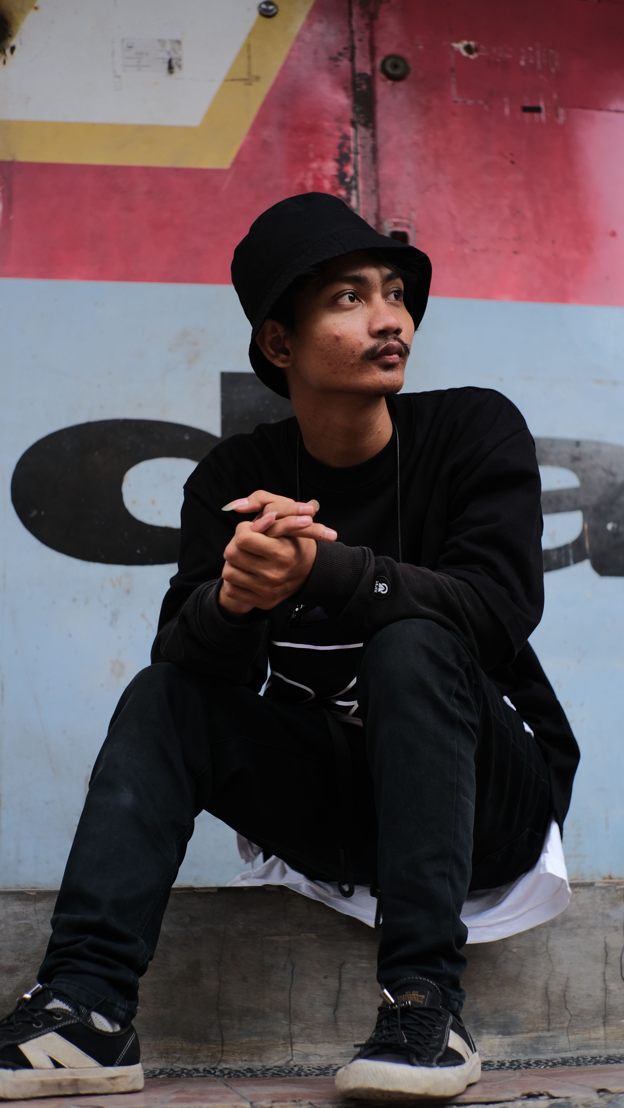 Street-style portrait of a man in casual black clothing, looking thoughtful.