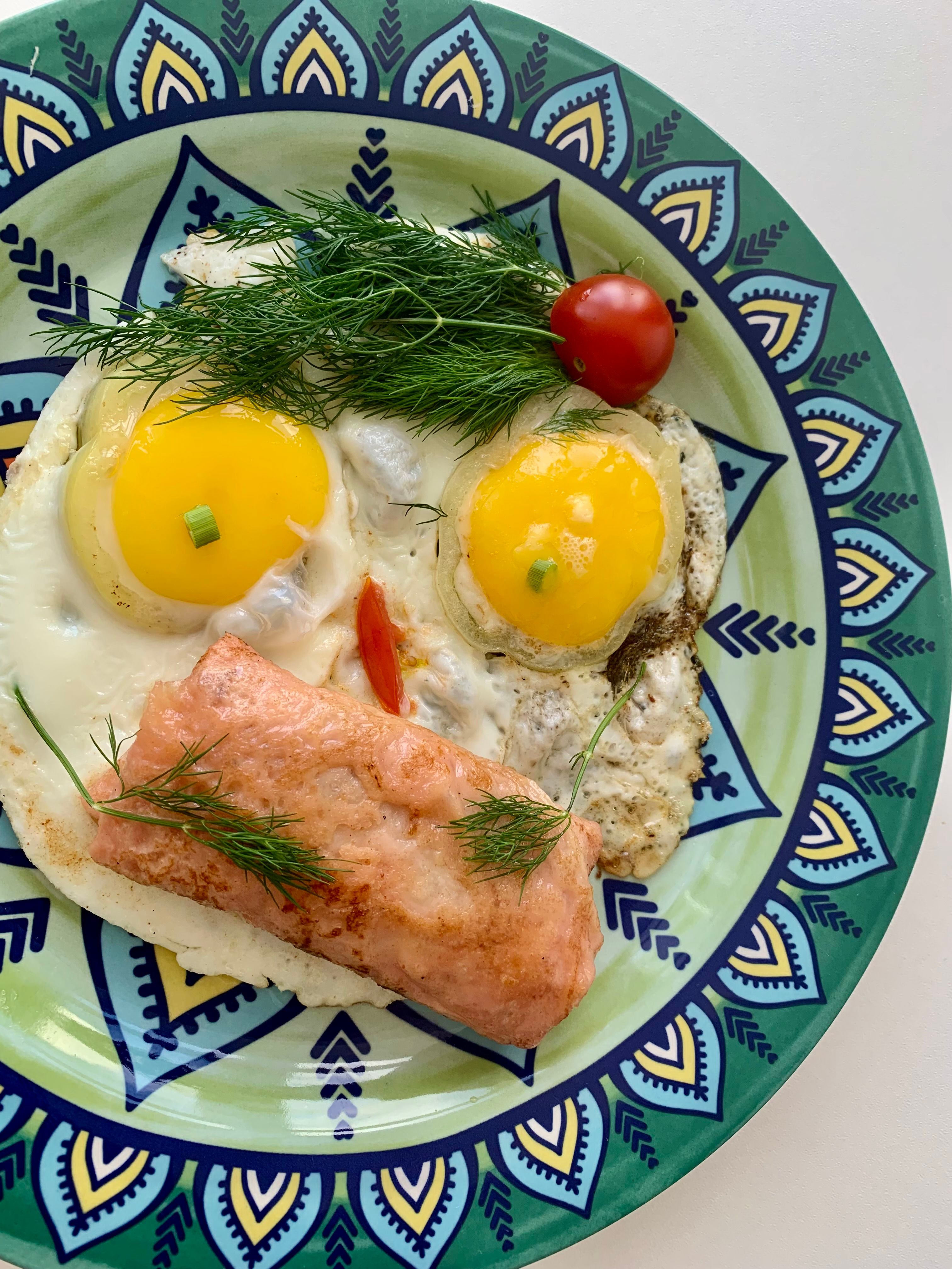 A vibrant breakfast plate featuring eggs, salmon, dill, and tomato.