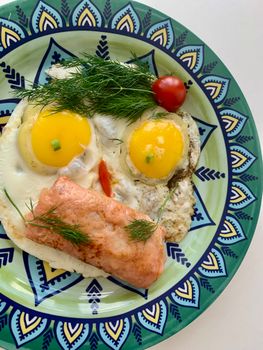 A vibrant breakfast plate featuring eggs, salmon, dill, and tomato.