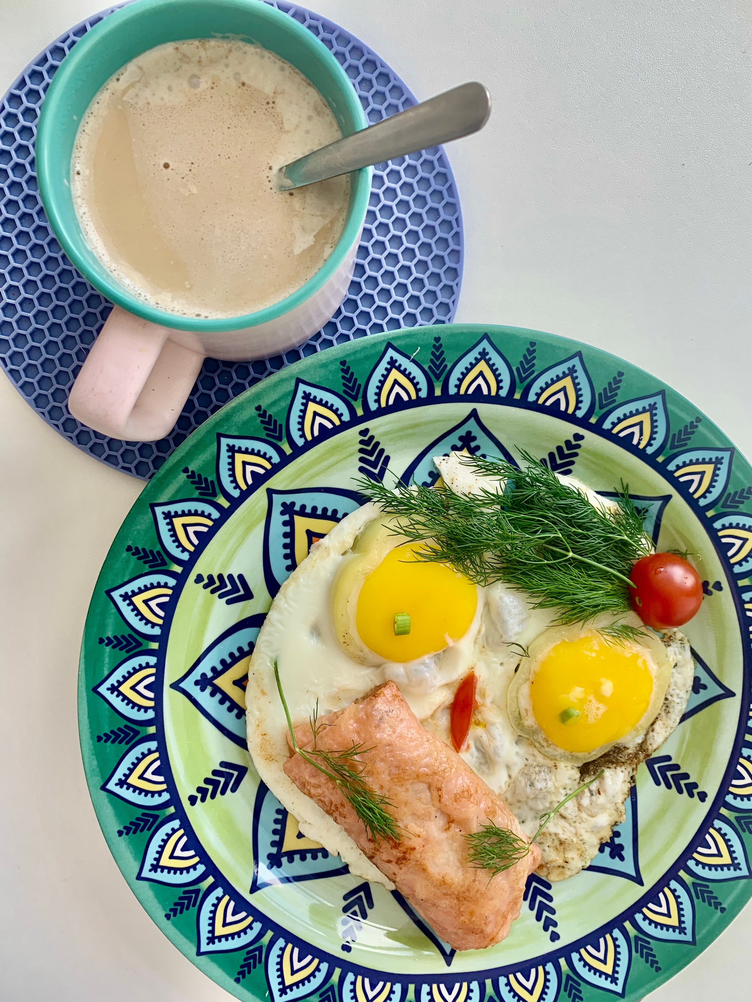 Vibrant breakfast with eggs, salmon, and coffee on colorful plates.
